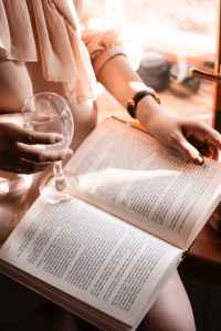 person holding wine glass while reading book